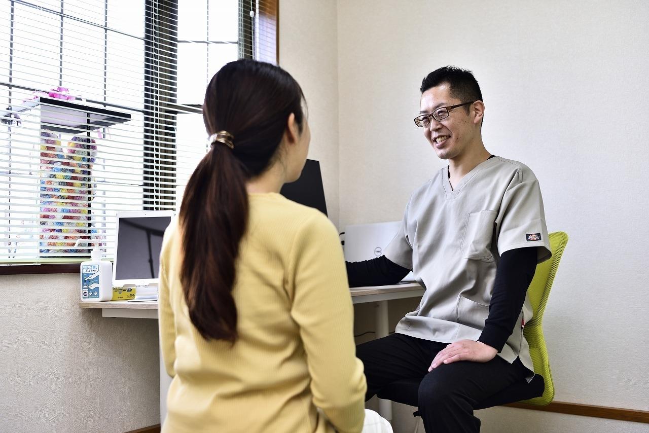 施術者がデスクで女性に問診しながら笑顔で説明している場面