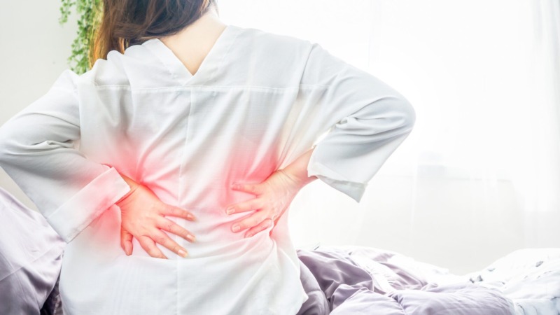 朝起きたら腰痛で動けず、布団の上で腰を押さえて悩む女性